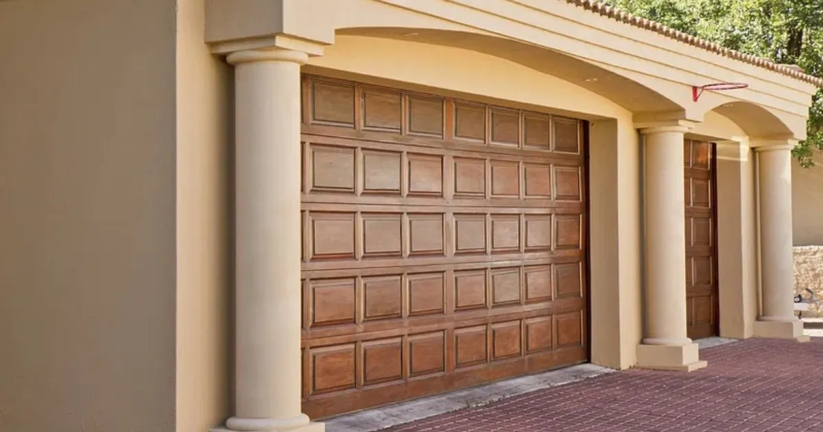 Broken garage door with visible dents and rusted hinges, preventing it from closing properly