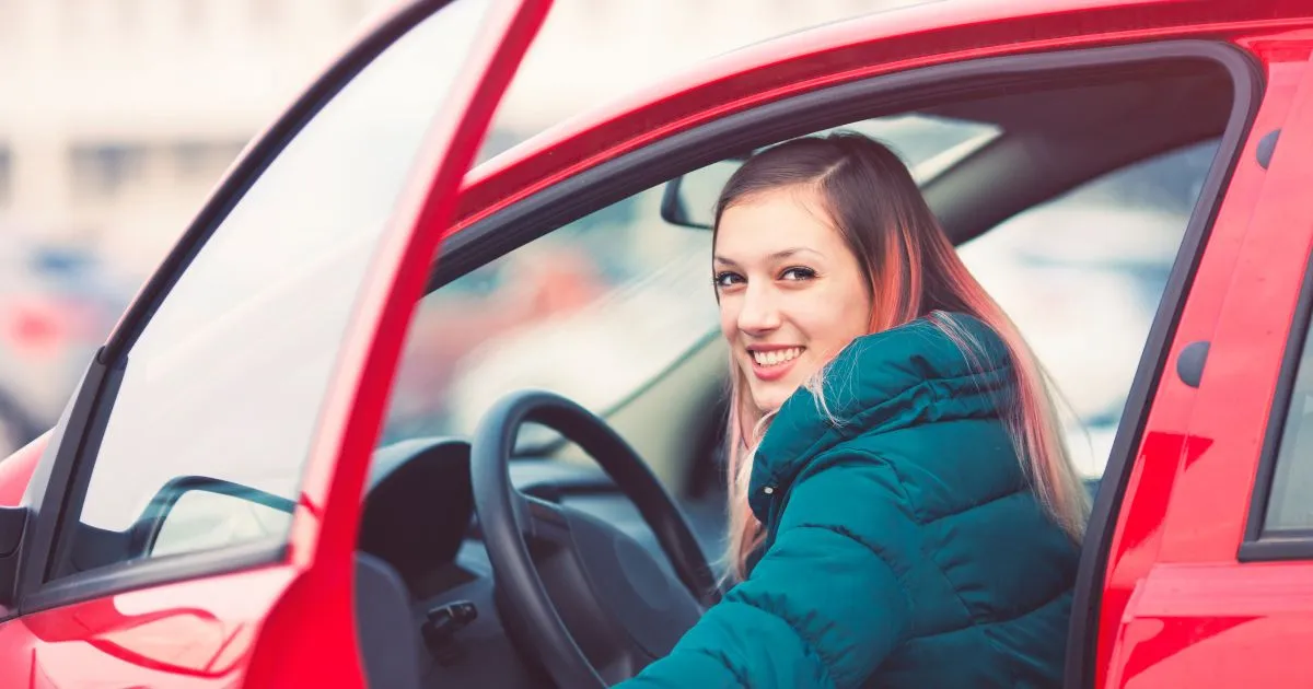 A Driver Posing After Parking Her Red Car In A Parking Lot