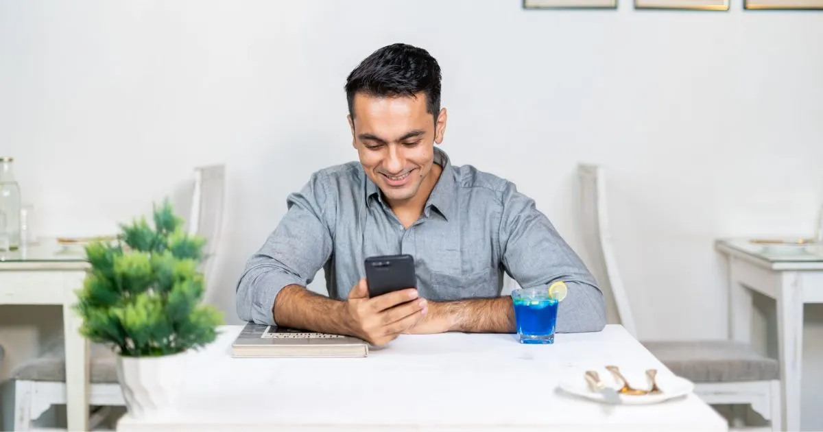 A Happy Young Man Looking At His Phone In A Cafe