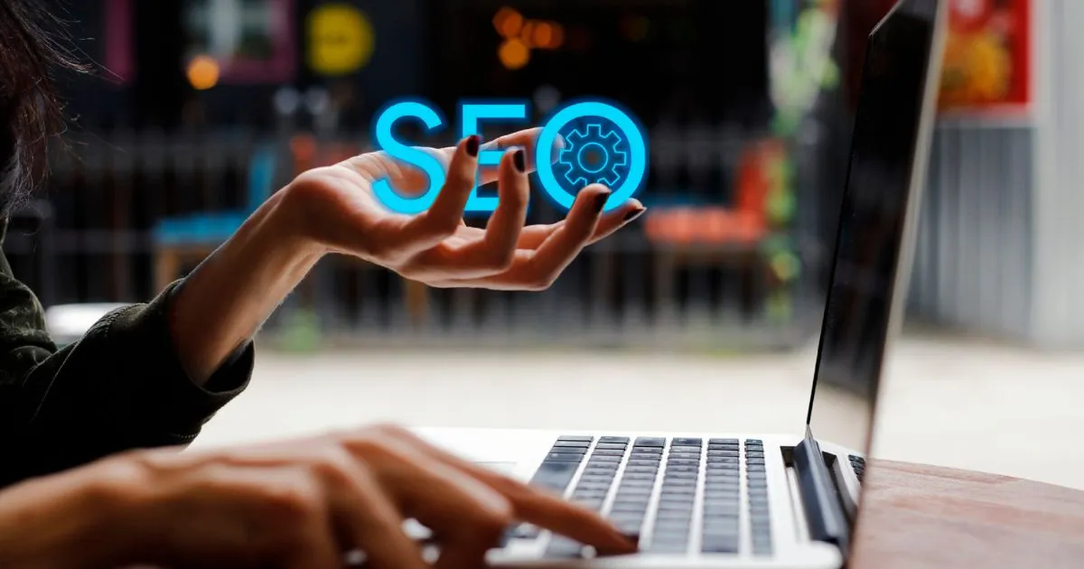 A Lady Working On Her Laptop With The Seo Monogram In Her Hand