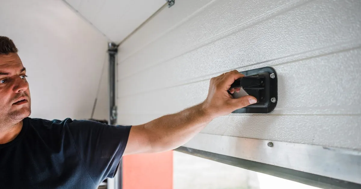A Man Installing A Sensing Device On His Garage Door To Make It More Secure