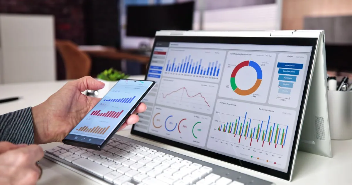 A Man Reviewing Multiple Charts On His Laptop And Smartphone