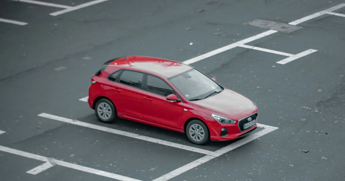 A Red Car Parked In An Uncovered Parking Lot With Many Empty Spaces Available For Booking
