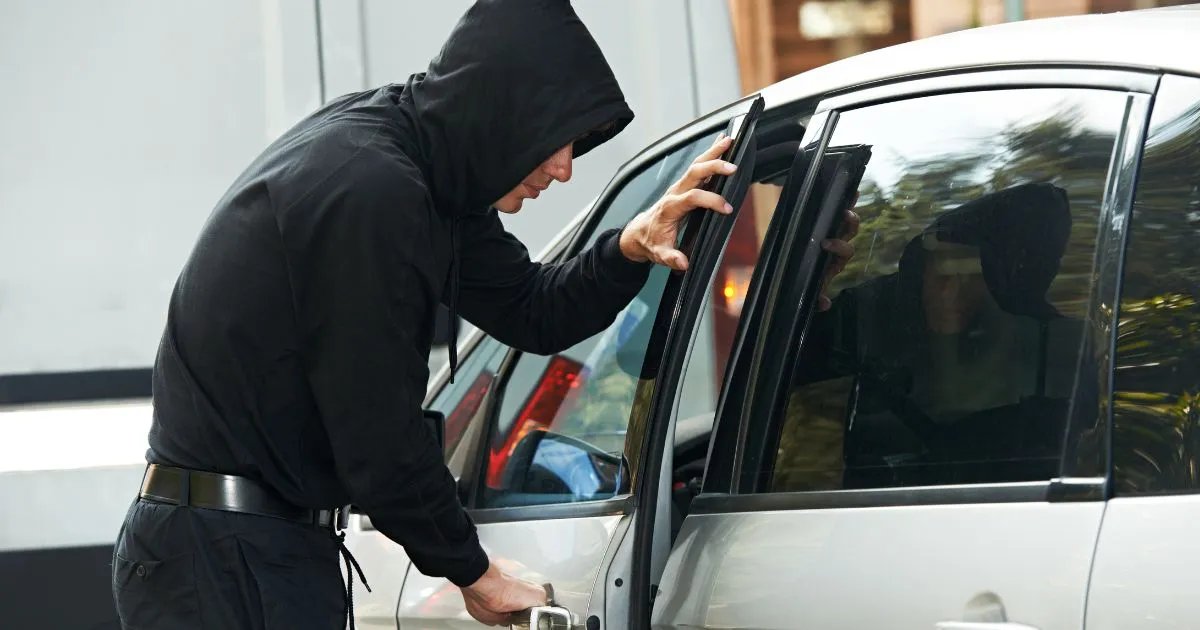 A Thief Unlocking A Luxury Car Parked In A Parking Lot