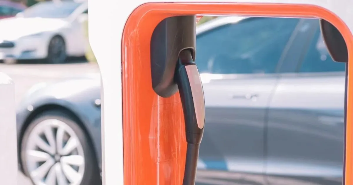 An Ev Charger At A Workplace With A Car In The Background