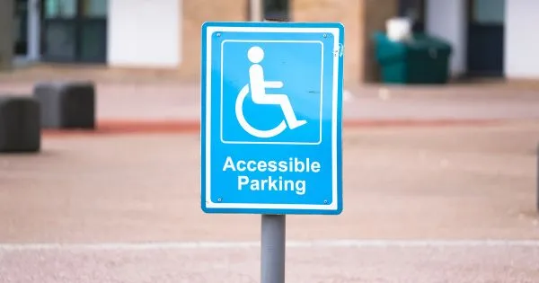 The Accessible Parking Sign On A Road With A Logo Of A Specially Able Person On A Wheelchair